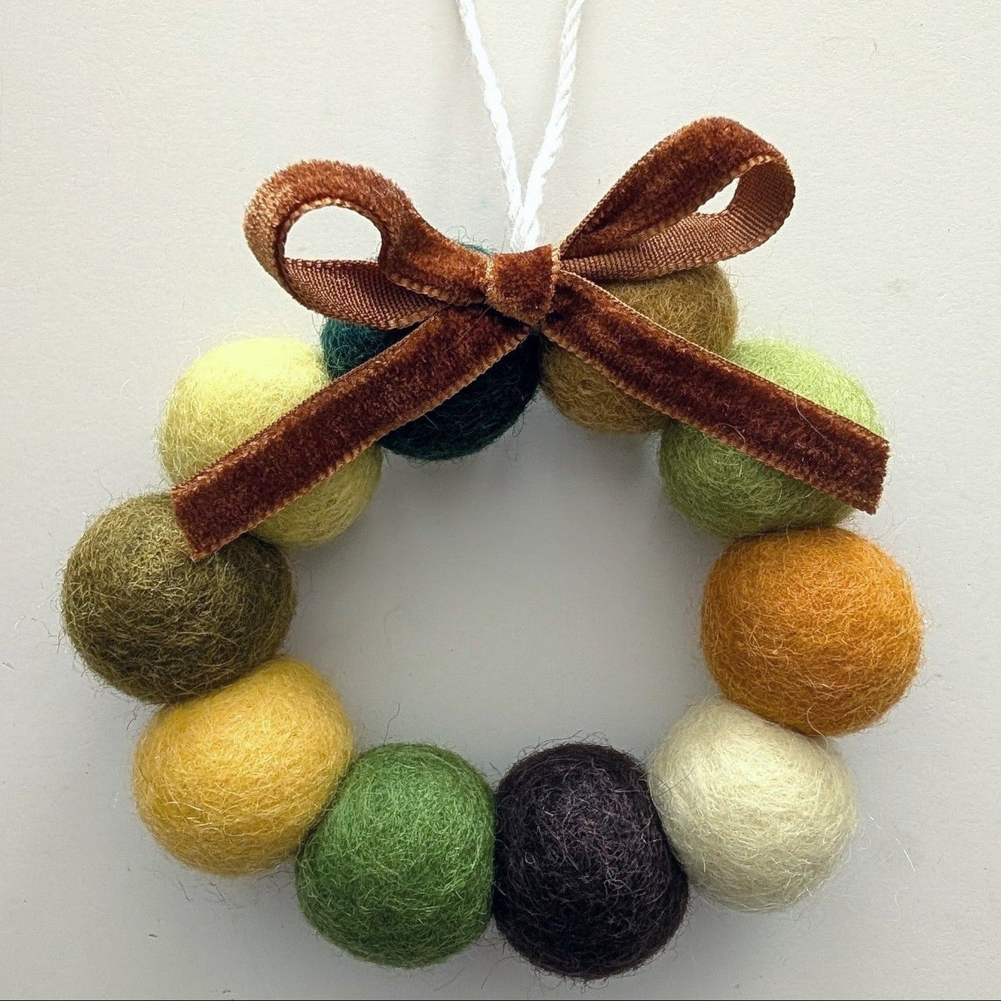 Decorative ornament with yellow, green, brown, and cream felt balls and a brown bow on a white background