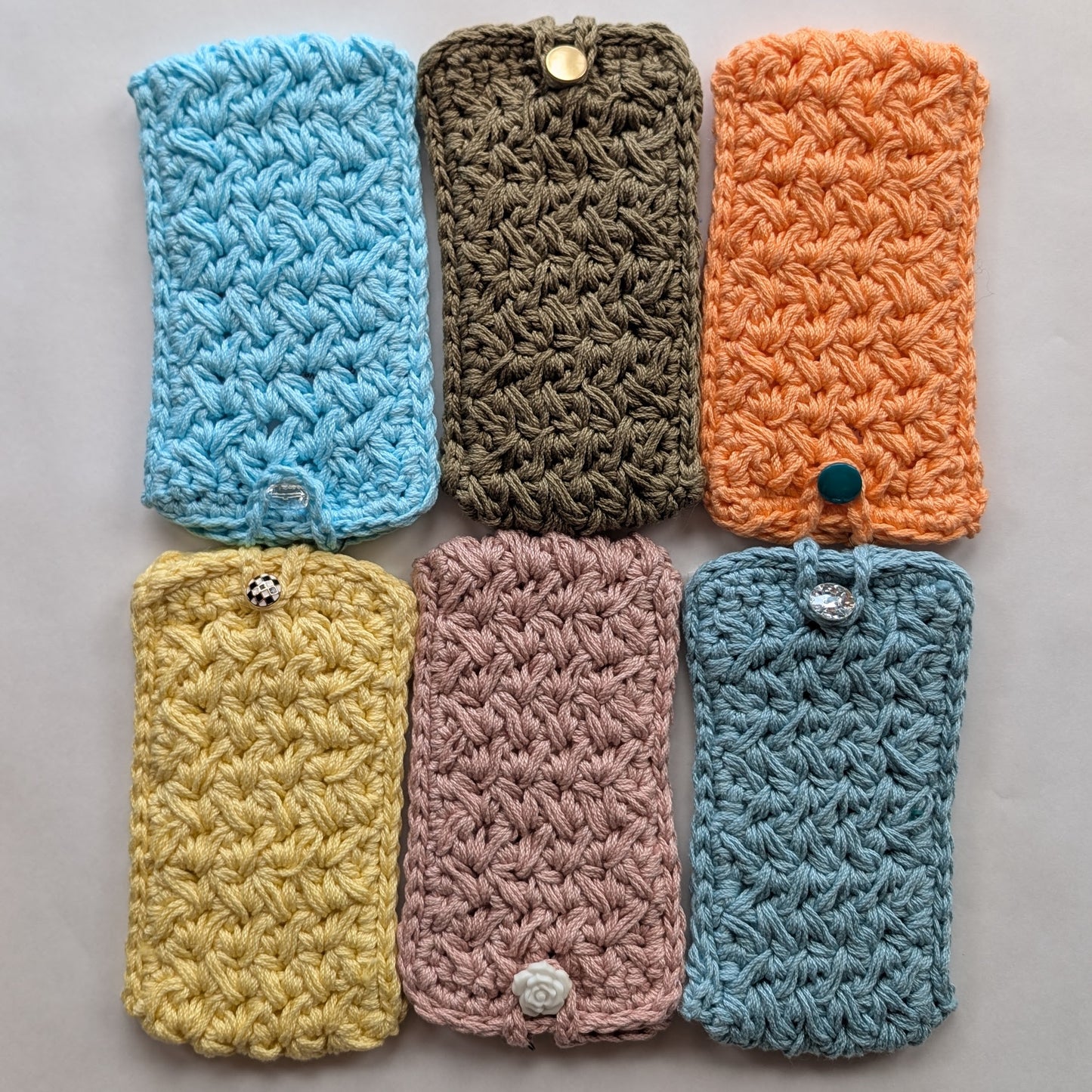 Six crocheted phone cases in various colors on a gray background