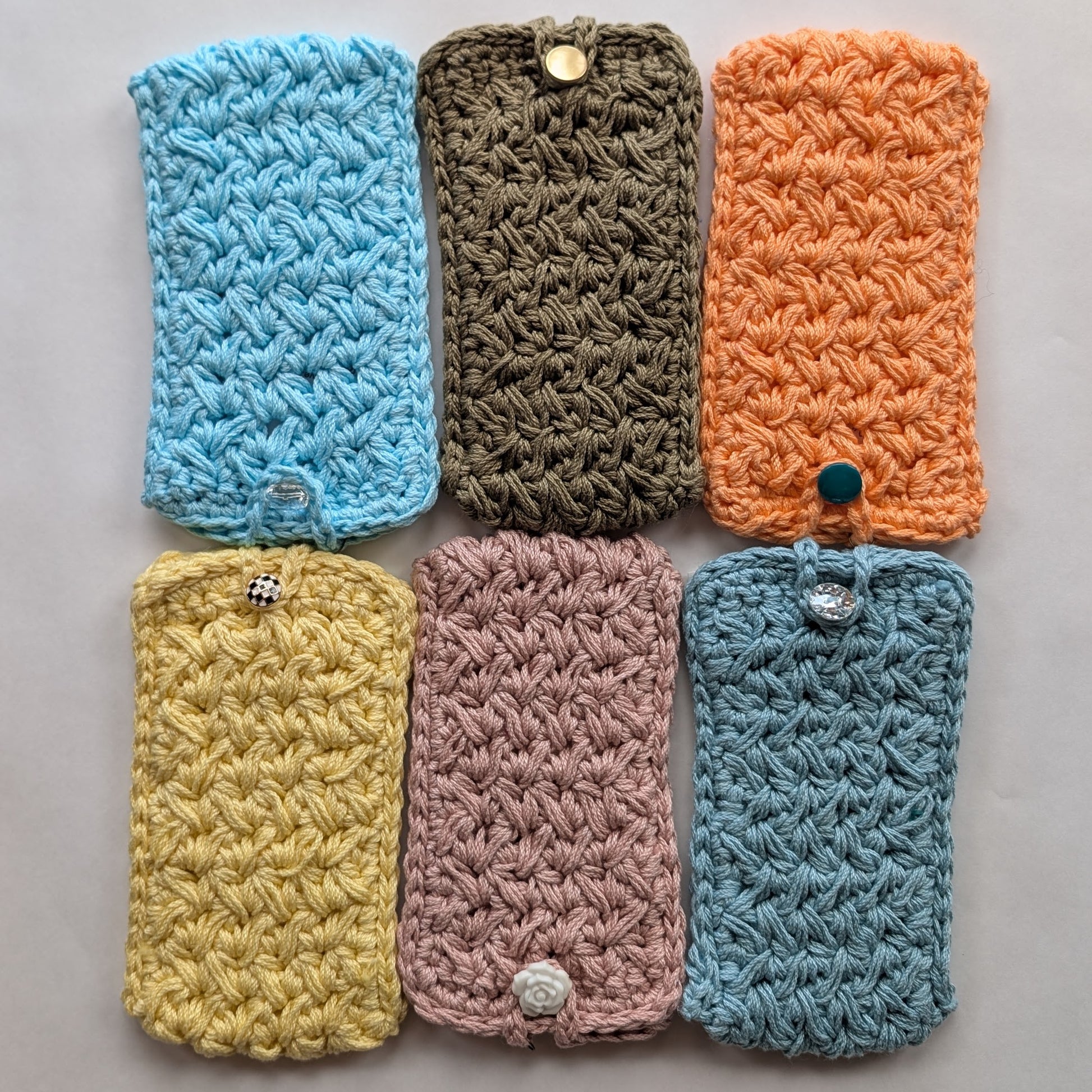 Six crocheted phone cases in various colors on a gray background