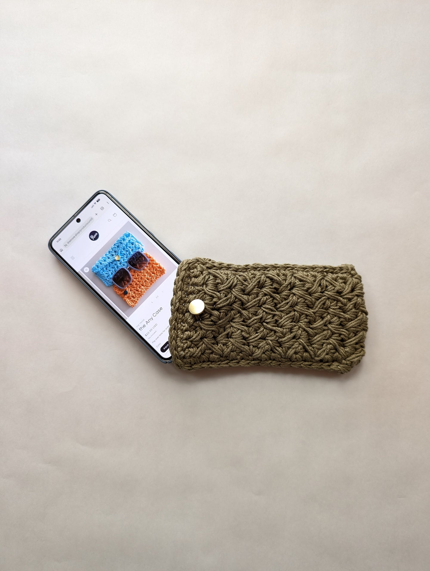 Green crocheted phone case next to a smartphone on a beige surface