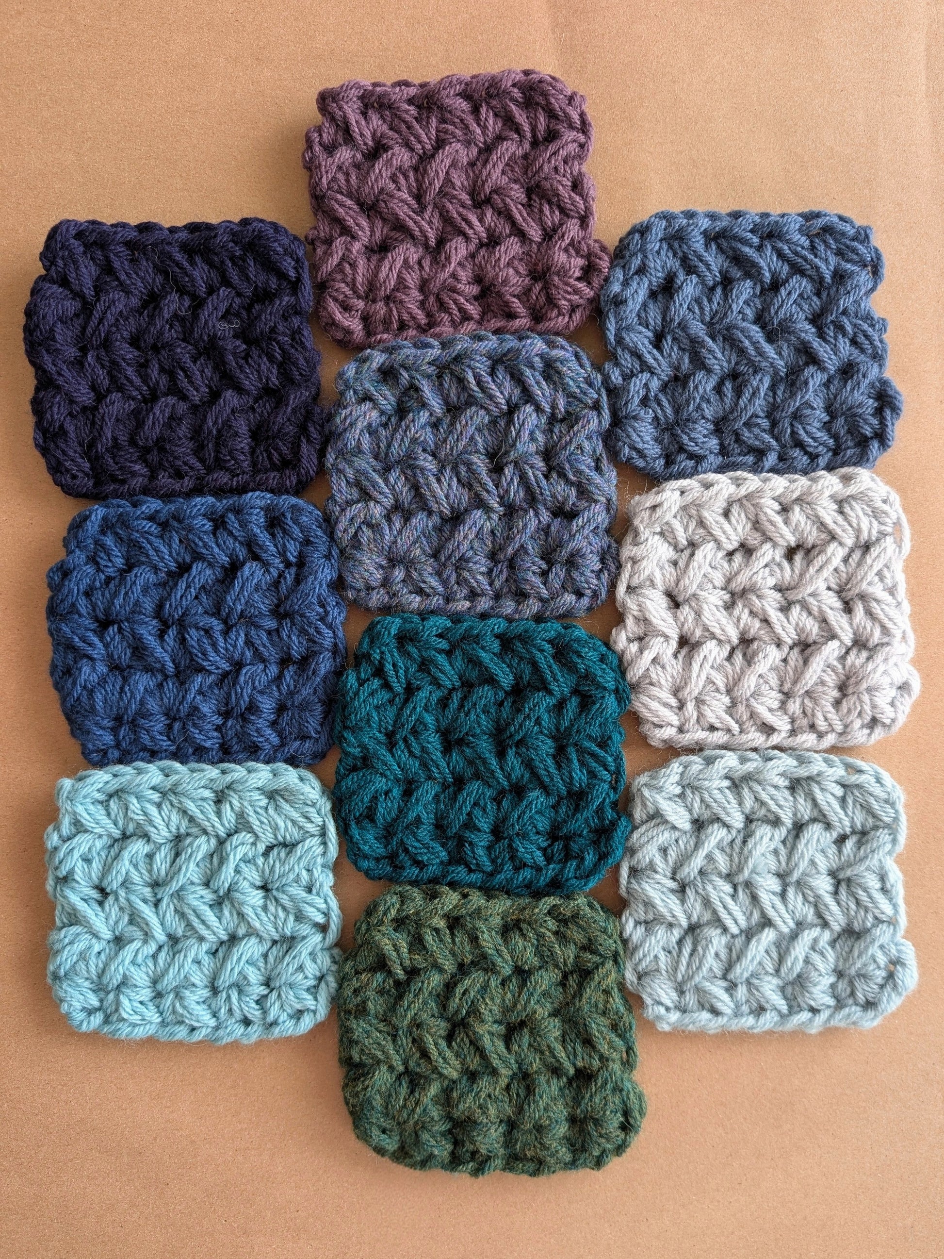 Ten crocheted squares in various shades of blue and green on a brown background.