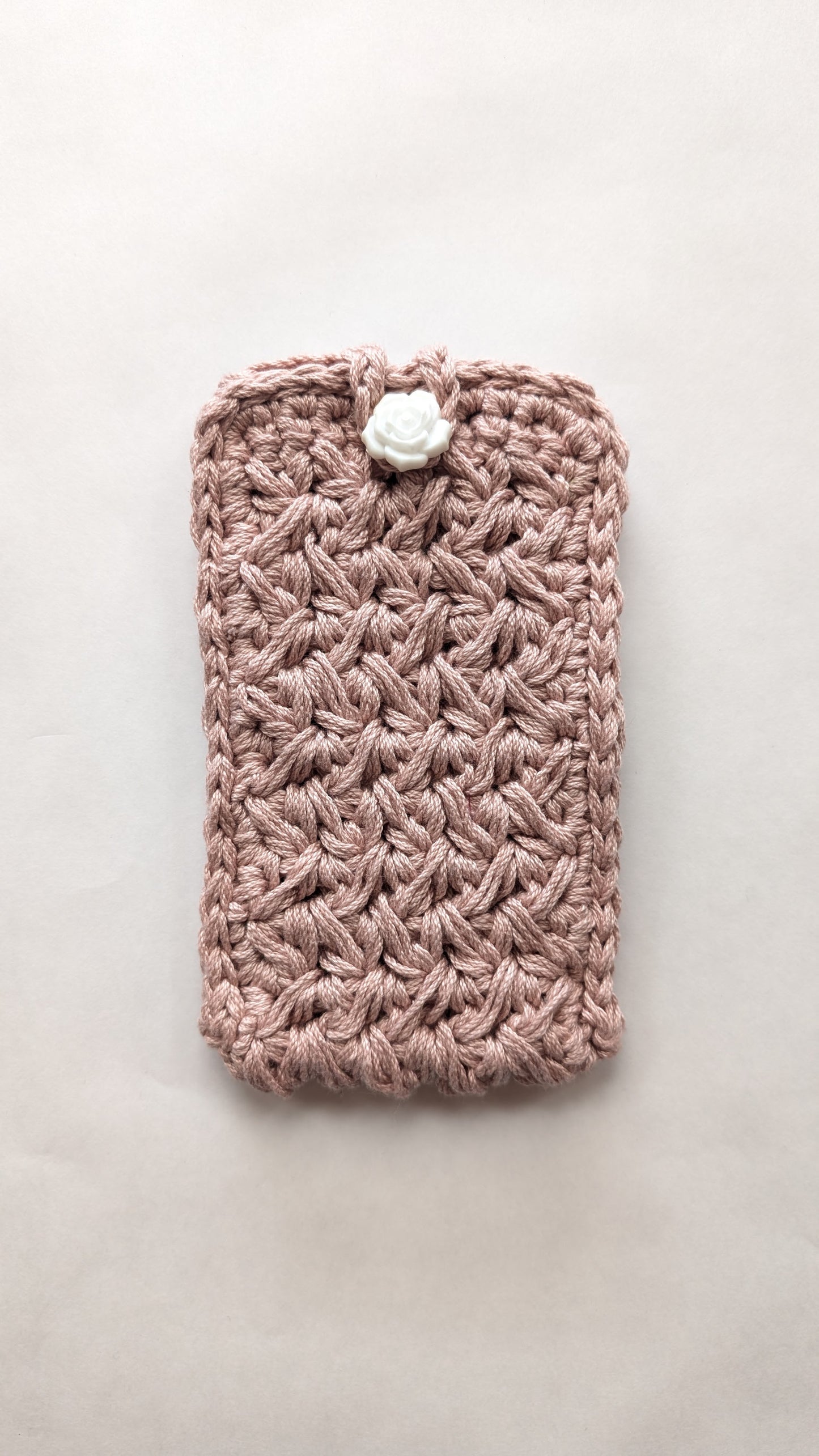 Pink crocheted phone case with a white button on a light gray background