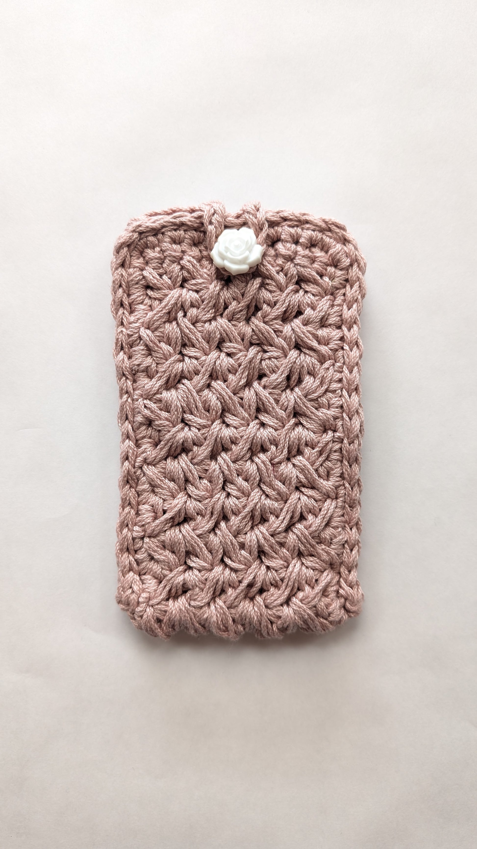 Pink crocheted phone case with a white button on a light gray background