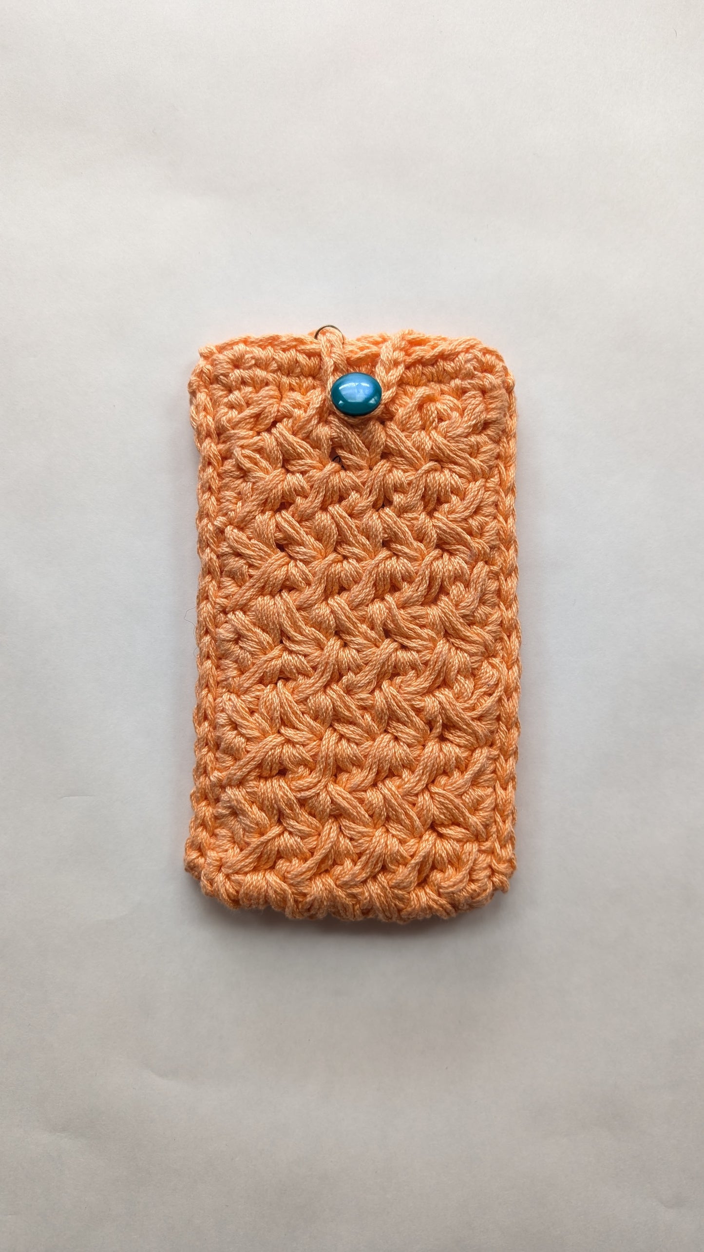 Orange crocheted pouch with a blue button on a light gray background