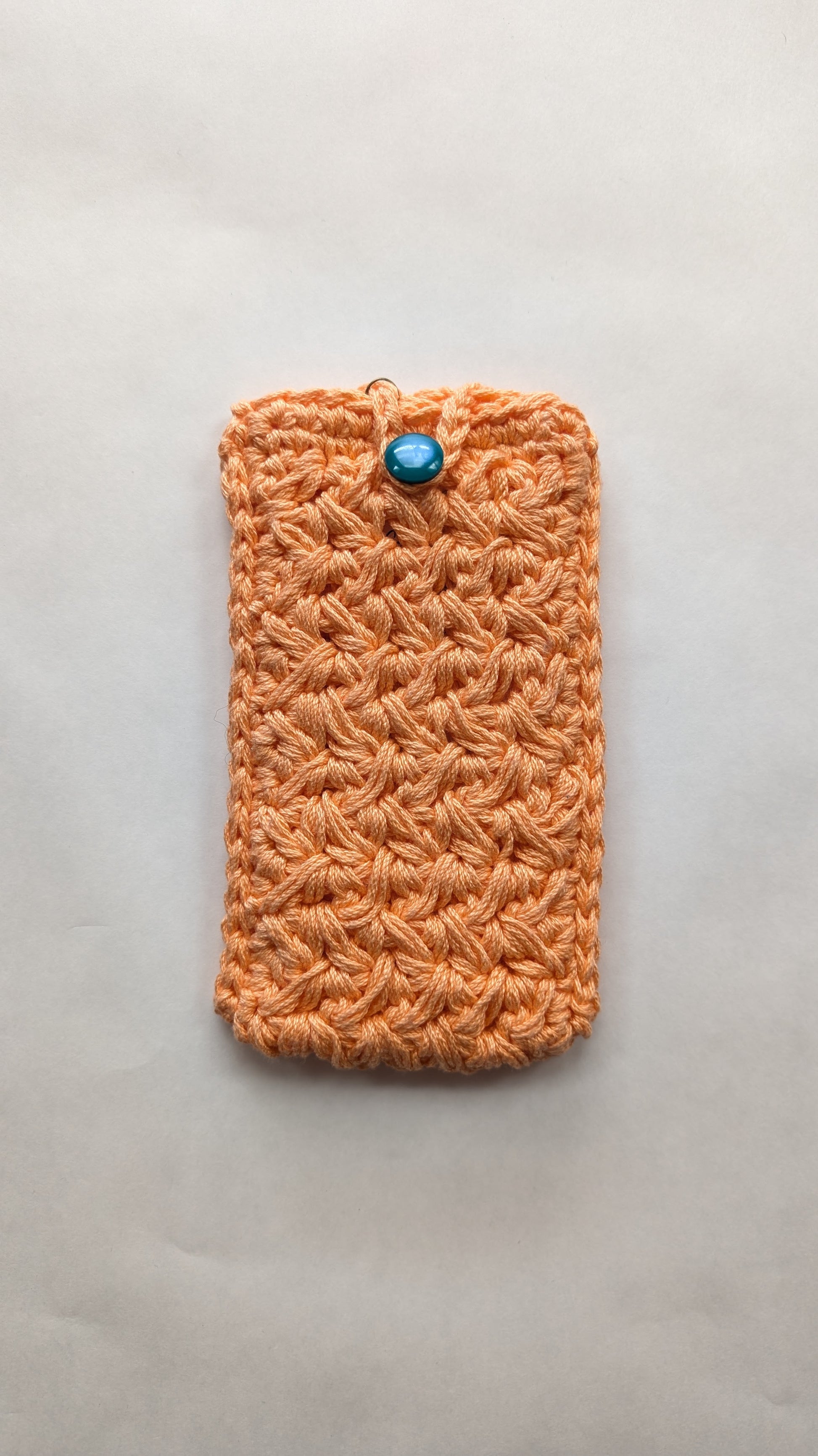 Orange crocheted pouch with a blue button on a light gray background