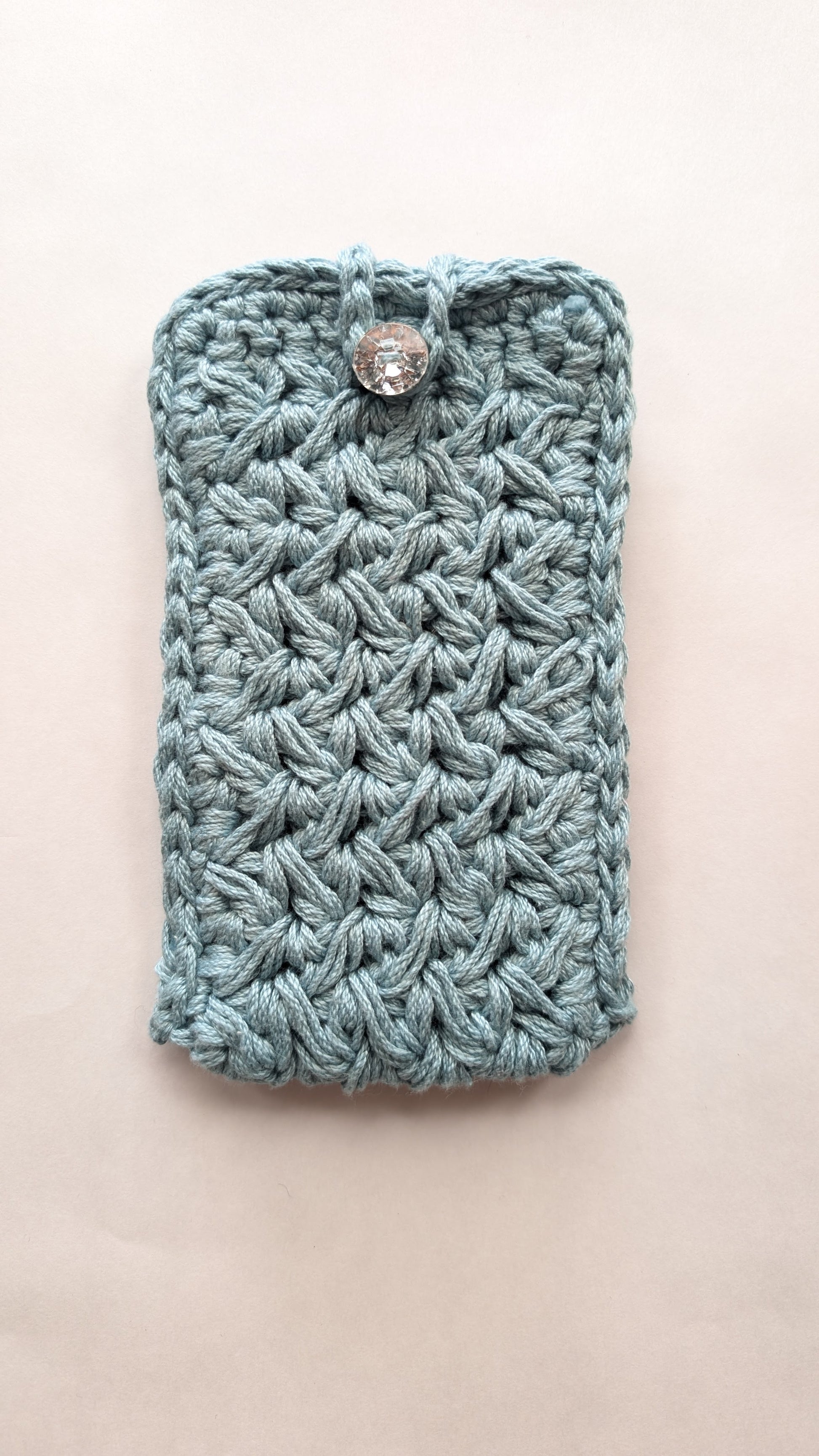 blue grey Crocheted phone case with a button on a beige background